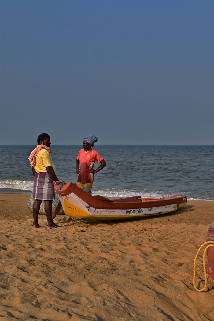 Fishermen stand by a boat on a serene Chennai beach, ready for the day.
